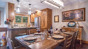 A spacious kitchen with wooden cabinets, a dining area set for six, and a large window providing natural light. - Elkhorn Ridge Condo + FREE Resort Amenities (Sun Valley)