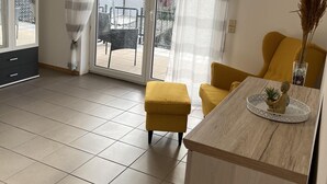 A modern living room with a yellow sofa, a wooden coffee table with a decorative item, and a sliding glass door leading to an outdoor area. - Sunset Apartment mit Rheinblick in Urbar (Urbar)