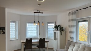 A modern living room with a sofa, a coffee table, a dining area with chairs, and a kitchen area with a cabinet. - Sunset Apartment mit Rheinblick in Urbar (Urbar)