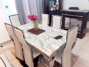 Una mesa de comedor con cubierta de mármol, rodeada de sillas blancas tapizadas. Un jarrón con flores rosadas está sobre la mesa.