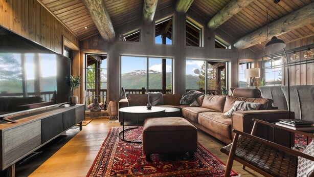 A spacious living room with a large window offering a mountain view, a cozy seating area with a brown leather sofa, a round coffee table, and a patterned rug. - Awesome home in Hornindal with WiFi (Hornindal)