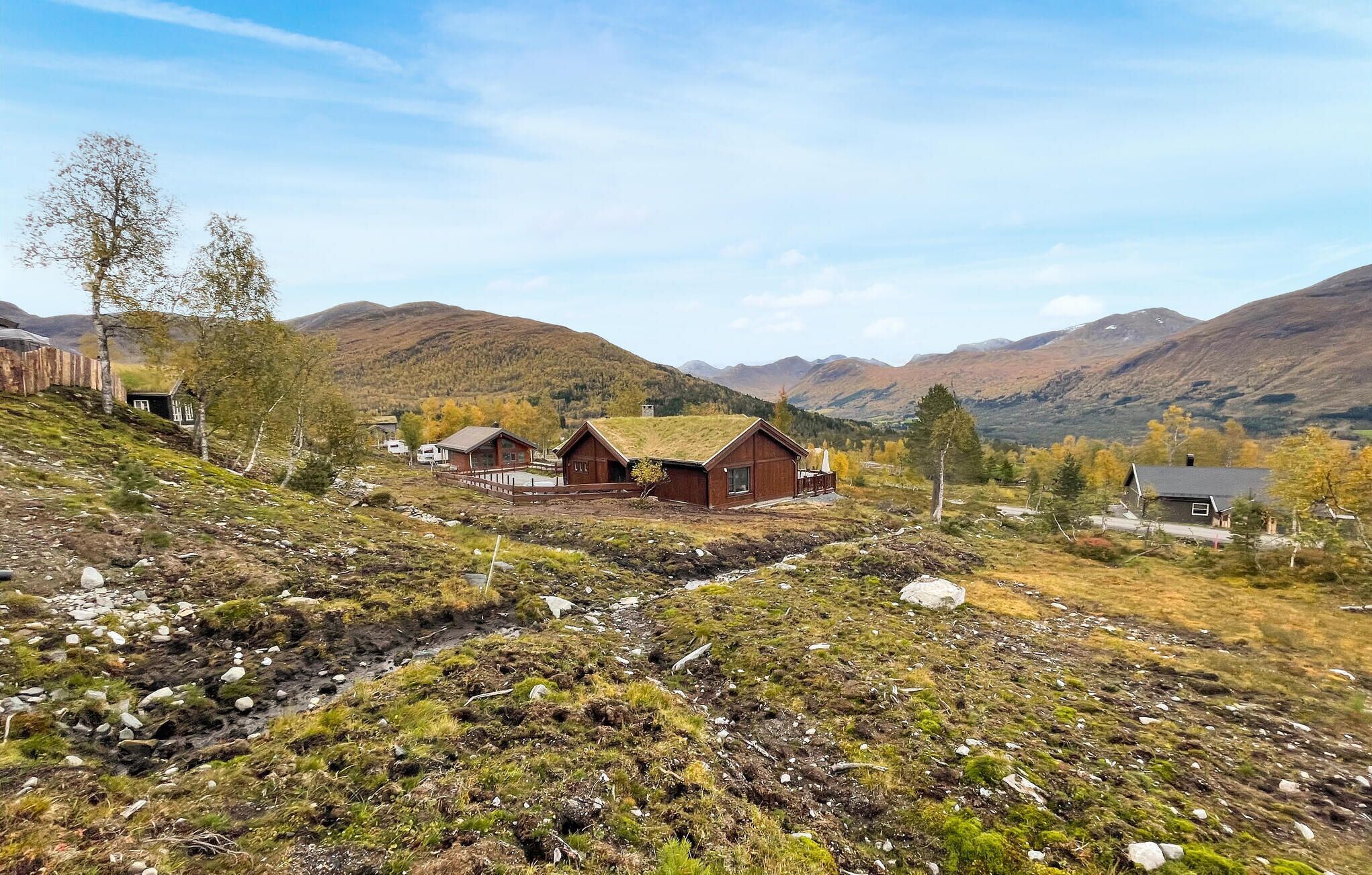 A remote cabin with a grassy roof, surrounded by mountains and sparse vegetation.