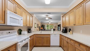 Une cuisine avec des meubles de rangement en bois, une cuisinière blanche, un four à micro-ondes, un lave-vaisselle et un ventilateur de plafond.