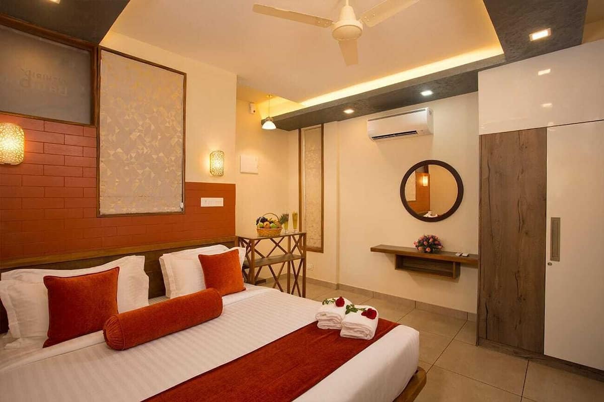 Habitación de hotel con una cama, un ventilador de techo, un aire acondicionado instalado en la pared, un espejo redondo y una pequeña mesa con una cesta.