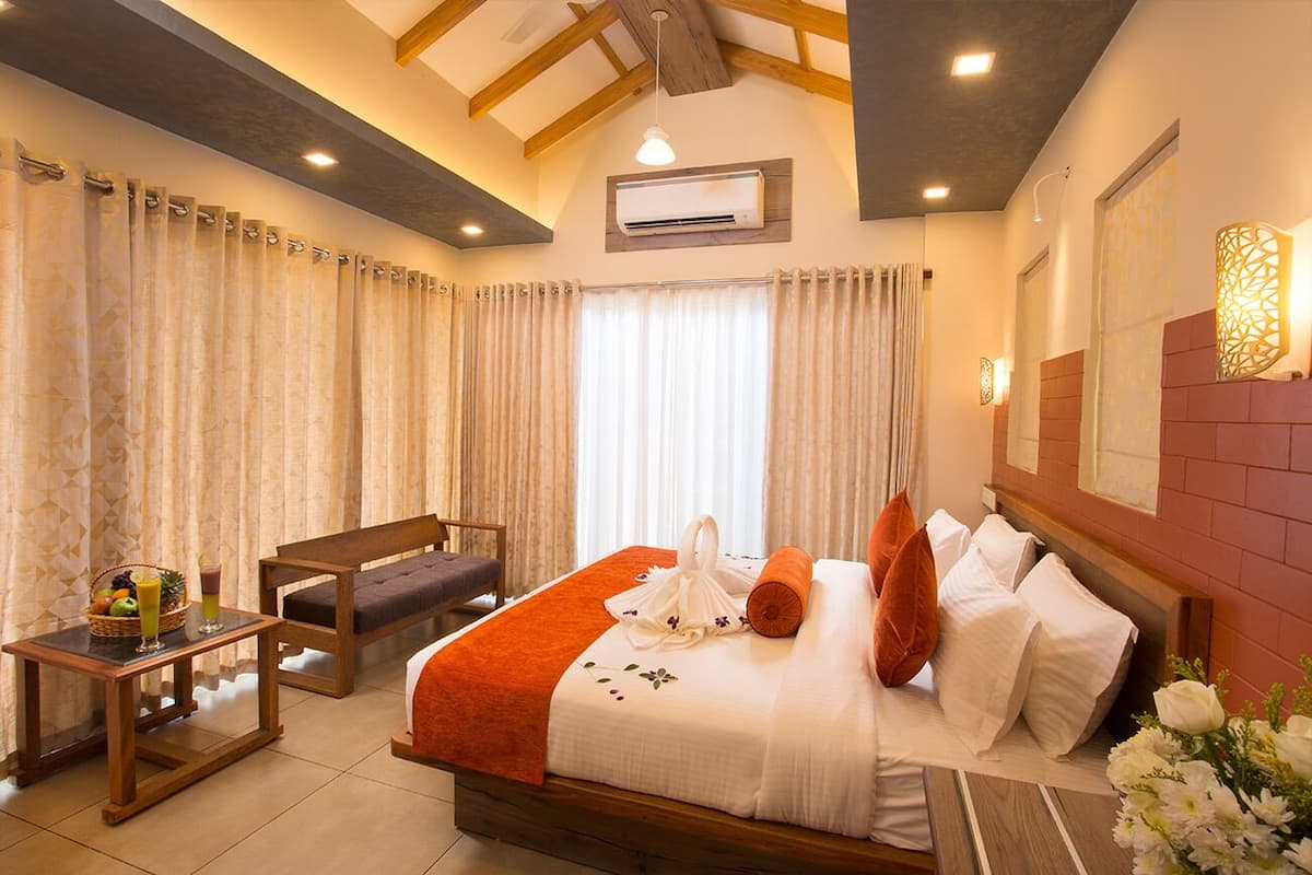 Habitación de hotel con cama, un banco, una mesa con frutero y aire acondicionado instalado en la pared.