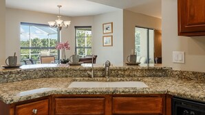 A kitchen with granite countertops, wooden cabinets, a stainless steel sink, and a chandelier. - Newly Renovated, Gulf Access & Heated Pool - Villa Following the Sun - Roelens Vacations (Cape Coral)