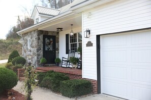 A house with a stone facade, a porch with chairs, a garage door, and a well-maintained garden. - Spacious Family Home w/ Fireplace & Fire Pit (Grayson)