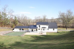 A two-story house with a covered patio, a lawn, and trees in the background. - Spacious Family Home w/ Fireplace & Fire Pit (Grayson)