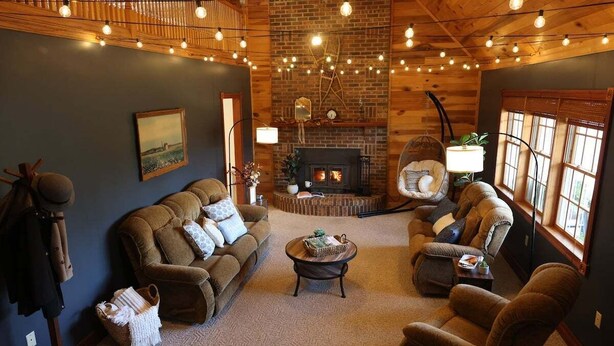 A cozy living room with a fireplace, a high ceiling with exposed beams, and a comfortable seating area. - Spacious Family Home w/ Fireplace & Fire Pit (Grayson)