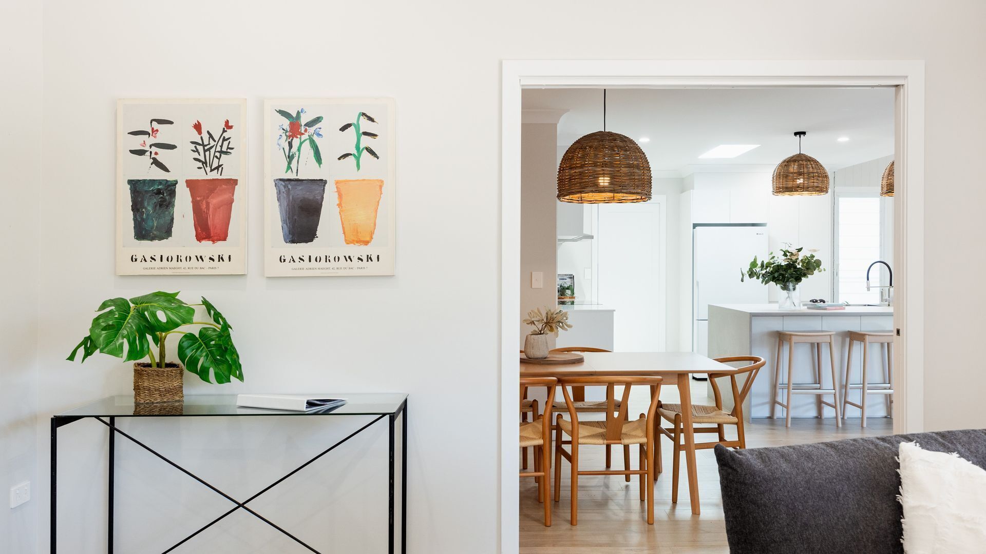 Una cocina moderna con armarios blancos, un comedor con sillas de madera y lámparas colgantes de mimbre.