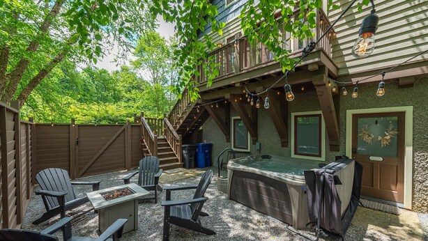 Un patio trasero con sillas Adirondack, un jacuzzi y una zona de parrilla cubierta.