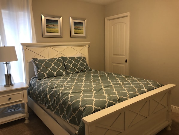 A bedroom with a bed, nightstand, lamp, and two framed pictures on the wall.