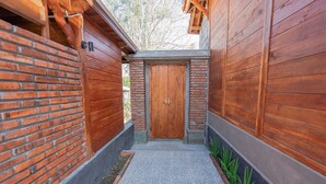 Un estrecho sendero que conduce a una puerta de madera, con un muro de ladrillo a un lado y un muro de madera al otro.