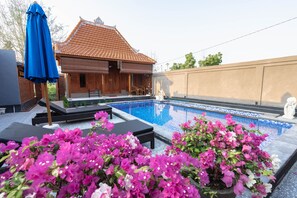 A swimming pool with lounge chairs and a blue umbrella, surrounded by vibrant pink flowers. - Garvi Villa (Karangasem)