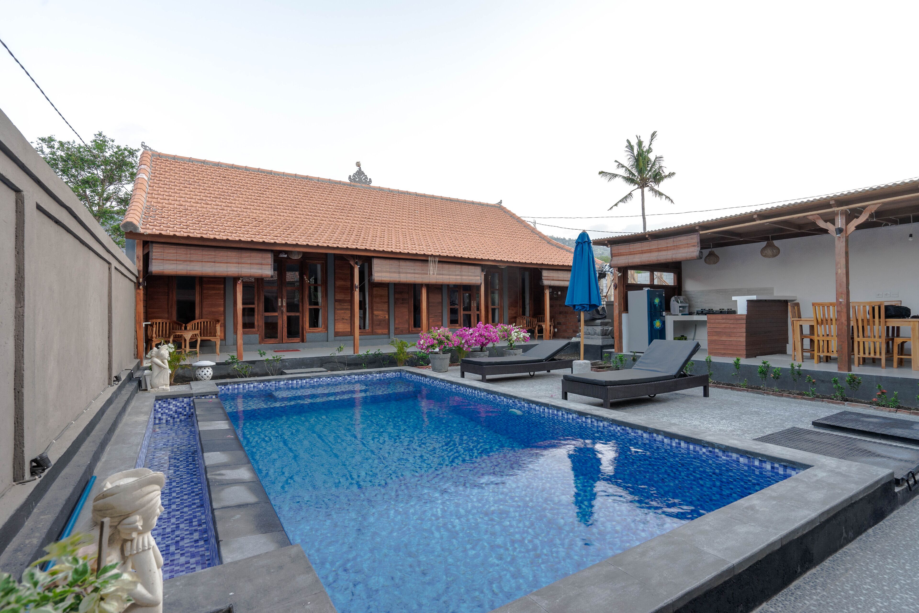 A swimming pool with a tiled deck, lounge chairs, and a covered seating area.