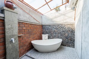 A modern bathroom with a freestanding bathtub, a brick wall, and a stone wall. - Garvi Villa (Karangasem)