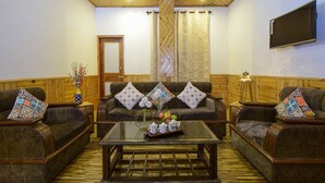 Una sala de estar acogedora con un conjunto de sofá, una mesa de centro con fruta y jarrones, y un televisor montado en la pared.
