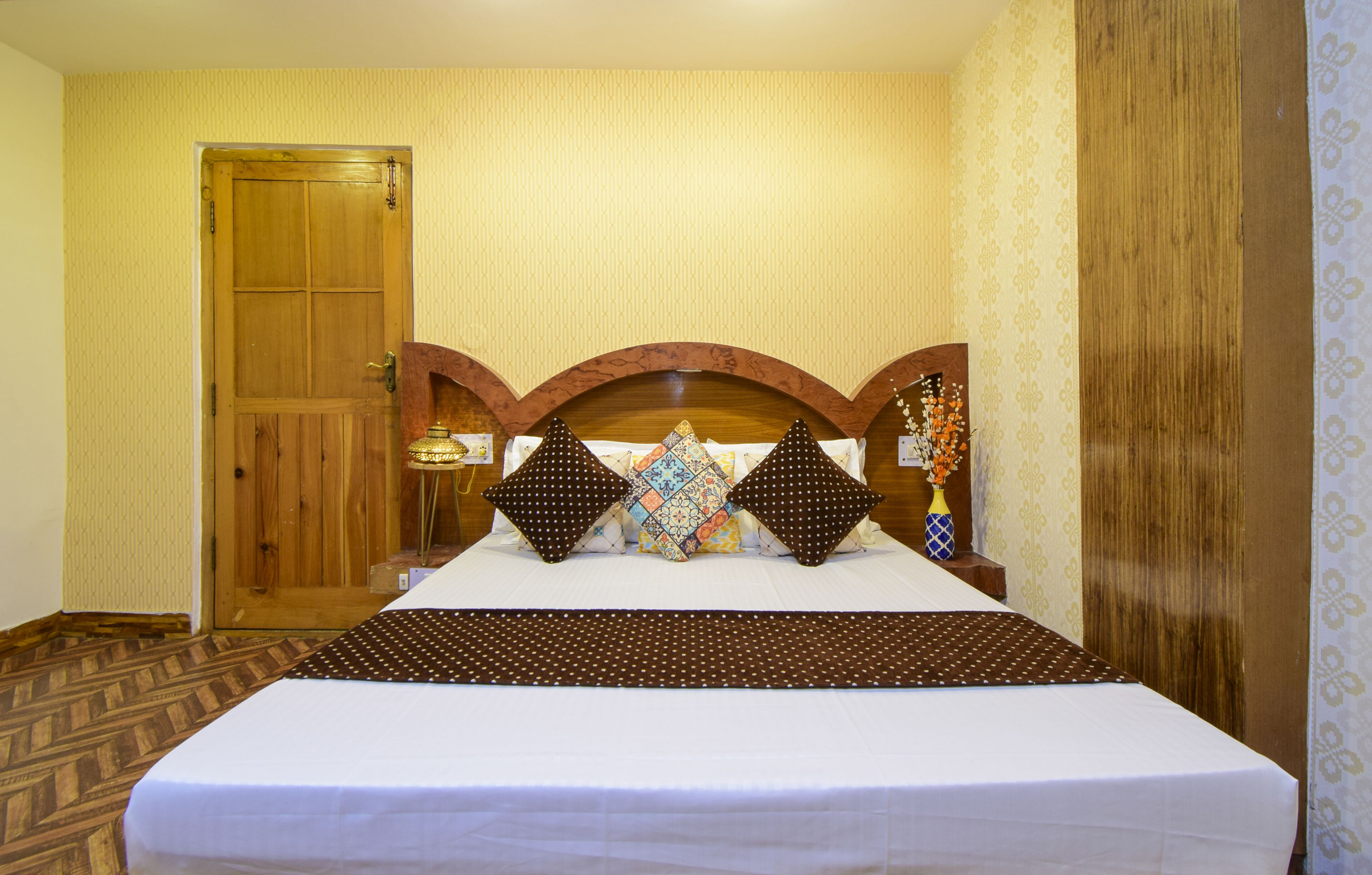 Une chambre d’hôtel avec une porte en bois, un lit doté d’une tête de lit à motifs et un mur orné de motifs.