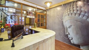 Un mostrador de recepción con una barra de madera, un sillón de cuero y un gran mural de Buda en la pared.