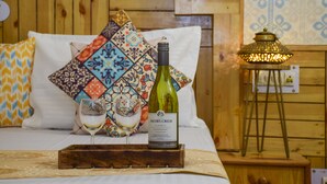 Una cama con cabecera de madera, un cojín colorido, una botella de Jacob's Creek Chardonnay y una copa de vino sobre una bandeja.
