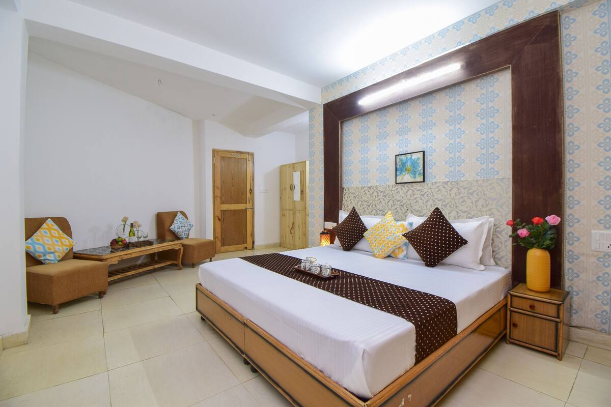 Un dormitorio amplio con una cama grande, una mesita de noche de madera, un tocador, un armario y una pequeña zona de estar con sofá y sillones.