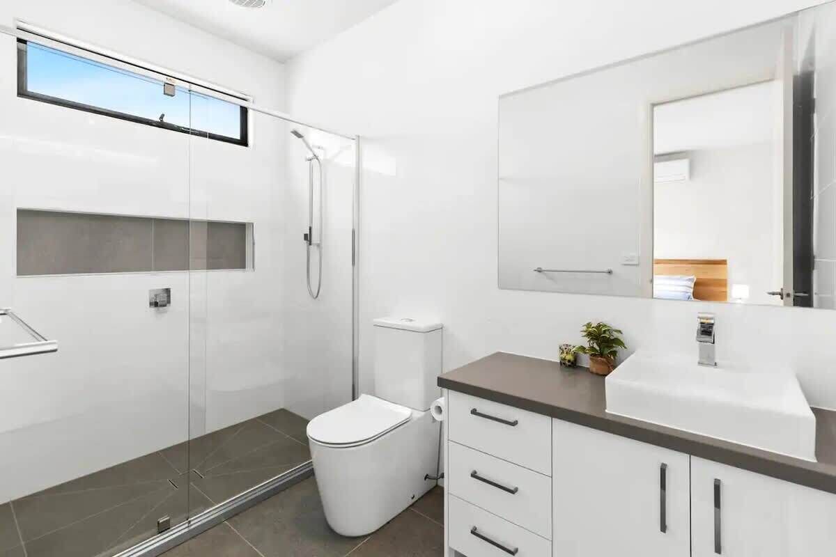 Un baño moderno con cabina de ducha de vidrio, inodoro, lavamanos con espejo y una pequeña planta en la encimera.