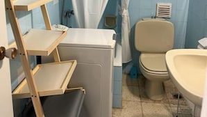 A bathroom with a white toilet, a sink, a shower curtain, and a wooden ladder. - Apartamento Canaleta (Punta Umbría)