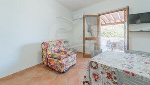 Une petite pièce avec une chaise à motifs floraux, une table recouverte d’une nappe à fleurs et un téléviseur fixé au mur.