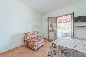A small room with a floral-patterned chair, a table with a floral tablecloth, and a TV on the wall.
