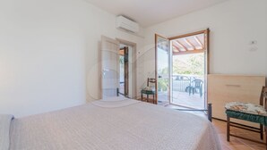 Une chambre à coucher comprenant un lit, une chaise et une porte-fenêtre coulissante donnant sur un espace extérieur avec une table et des chaises.