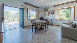 Amplia habitaci ón con una mesa de comedor rodeada de sillas, un sofá y grandes ventanales con vistas a la vegetación.