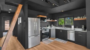 A modern kitchen with black cabinetry, stainless steel appliances, and a wooden floor. - Cozy Aframe Cabin Zen Near Zion (Glendale)