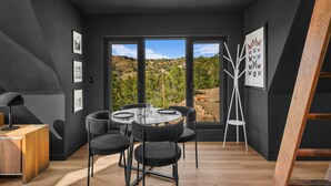 A modern dining area with a round table, black chairs, and a view of a mountainous landscape through large windows. - Cozy Aframe Cabin Zen Near Zion (Glendale)