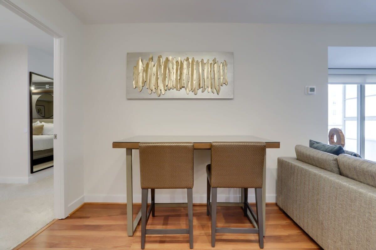 Un salon moderne avec un coin repas comprenant une table en bois et deux chaises. Une grande œuvre d’art abstraite est accrochée au mur, au-dessus de la table.