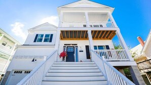 A two-story white building with a balcony on the second floor, a front door, and a staircase leading to the entrance. - Sojourn on Lea View | Willoughby Spit | 5 BR *NEW* (Norfolk)