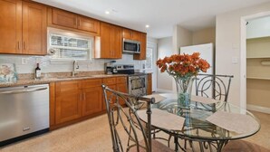 Una cocina moderna con armarios de madera, electrodomésticos de acero inoxidable y una mesa de comedor de vidrio con sillas de metal.