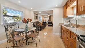 Una cocina moderna con encimeras de granito, armarios de madera y un comedor con mesa de vidrio y sillas metálicas.