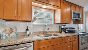 Una cocina con gabinetes de madera, encimera de granito, electrodomésticos de acero inoxidable y una ventana con persianas.