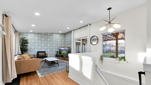 Un salon moderne avec un canapé, une table basse et un téléviseur, un escalier avec une rampe et une grande fenêtre donnant sur l’extérieur.