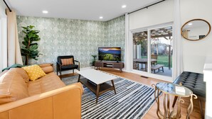 Un salon moderne avec un canapé, un téléviseur et une grande fenêtre donnant sur un jardin.