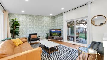 Un salon moderne avec un canapé, un téléviseur et une grande fenêtre donnant sur un jardin.