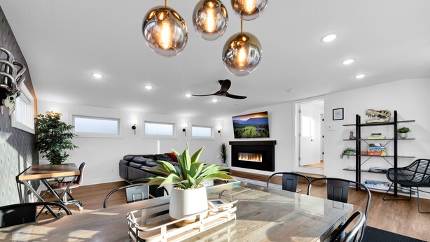 Un salon moderne avec une table à manger en bois, des chaises noires, une table avec un plateau en verre, un ventilateur de plafond et une cheminée.
