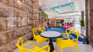 An indoor swimming pool area with a stone wall, yellow chairs, and a table. - 126 Vung Tau Pool Villa Back Beach (Ho Chi Minh City)