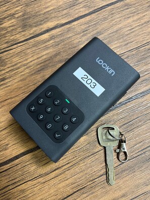 A black LOCKIN calculator with a display showing the number 203, placed on a wooden surface next to a key. - Yuzawa House (Yuzawa)