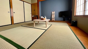 Una habitación al estilo japonés tradicional, con esteras de tatami, una mesa baja, un televisor y puertas correderas.