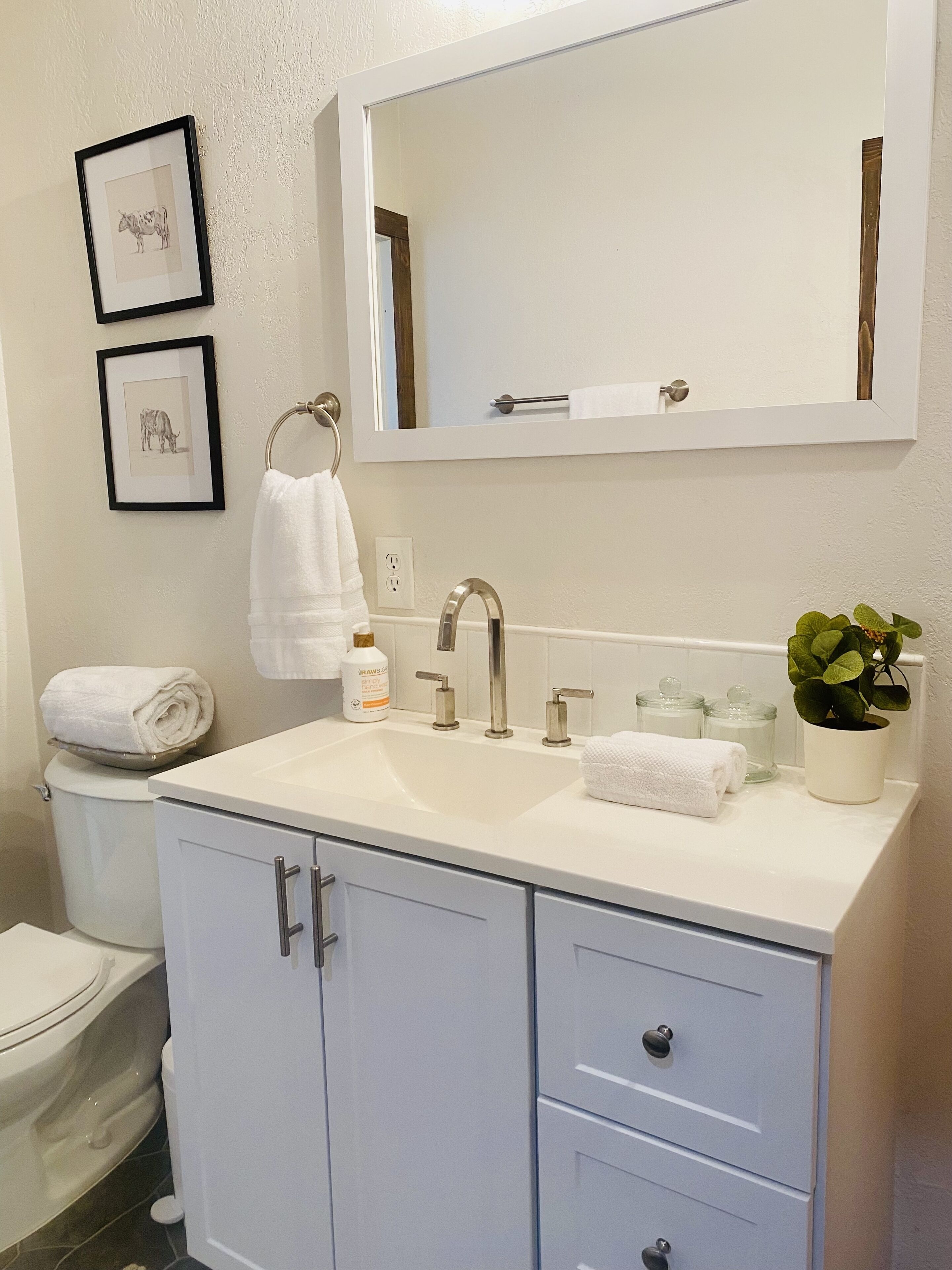 Un bagno con un lavandino bianco, uno specchio, un water e un mobile con cassetti.