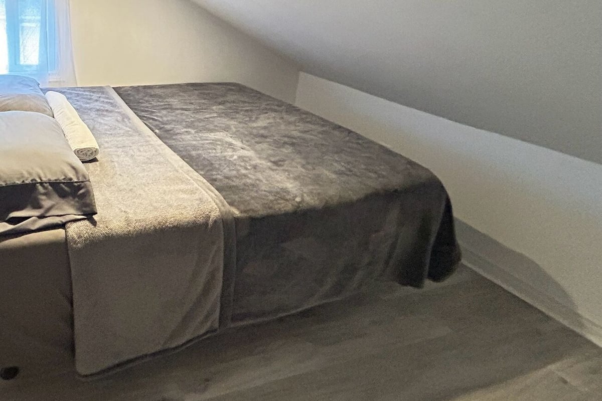 A small, dimly lit room with a single bed covered in a grey blanket.