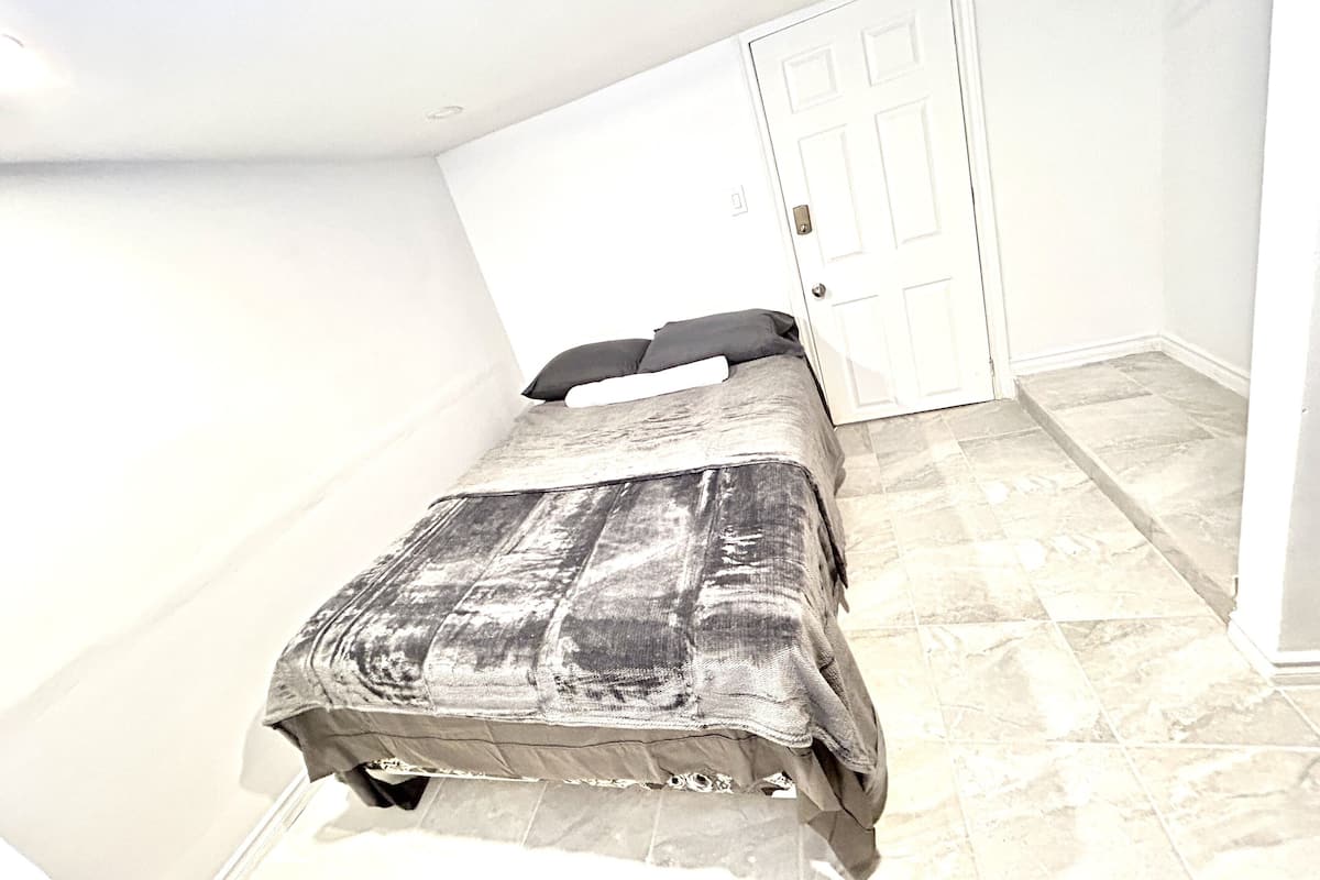A small, single-bed room with a sloped ceiling, a white door, and a tiled floor.