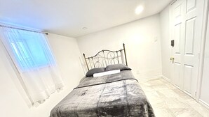 A neatly arranged bedroom with a bed, a window with sheer curtains, and a door. - Aubin Paradise (Windsor)