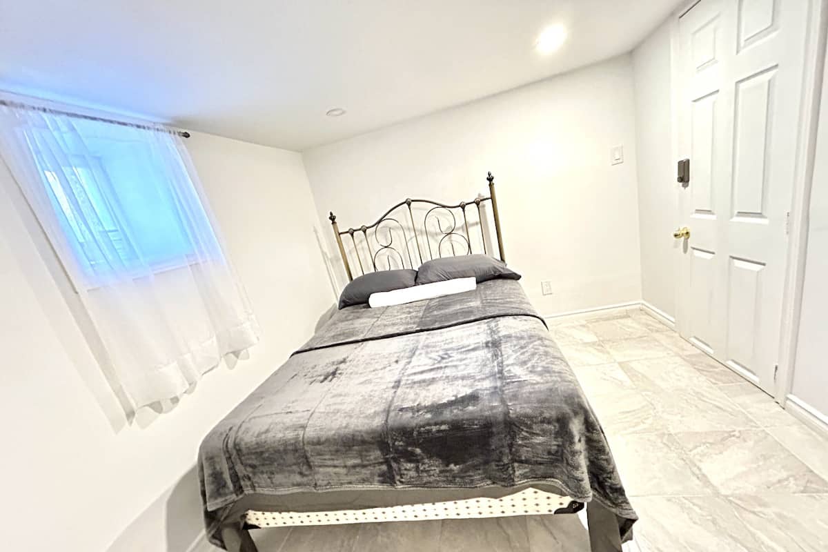 A neatly arranged bedroom with a bed, a window with sheer curtains, and a door.